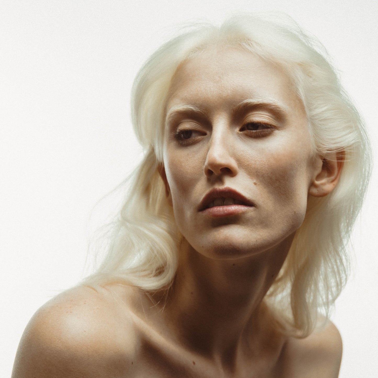Une jeune femme aux cheveux décolorés pose avec élégance pour mettre en avant la brume mémoire, le spray hydratant texturisant de la gamme. Ses cheveux sont légèrement en mouvement, avec un volume naturel en racine. Cette image incarne la beauté et la vitalité des cheveux grâce à l'utilisation de la brume mémoire.