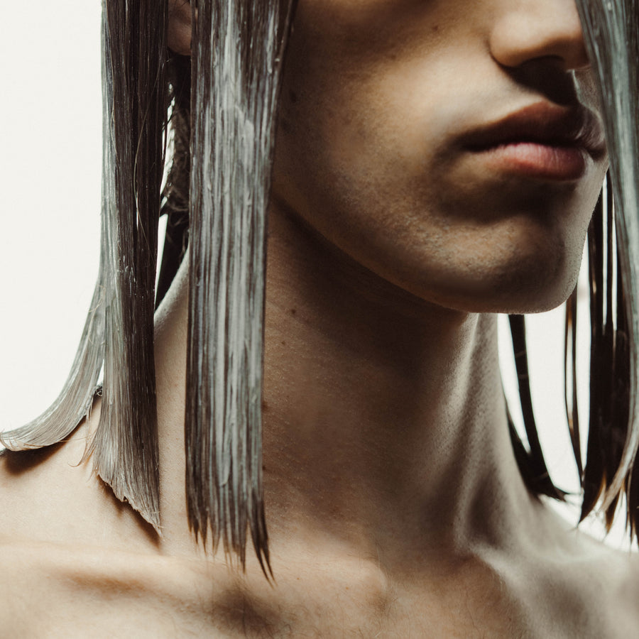 Un jeune homme aux cheveux longs pose avec élégance, tenant la crème de soin pour les longueurs et les pointes de ses cheveux. Cette photo met en avant l'utilisation du produit pour maintenir et nourrir les longueurs et les pointes de ses cheveux, pour un look soigné et sain.