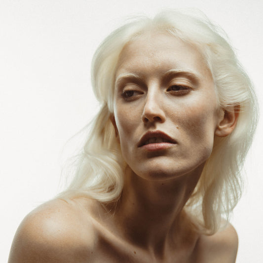 Une jeune femme aux cheveux décolorés pose avec élégance pour mettre en avant la brume mémoire, le spray hydratant texturisant de la gamme. Ses cheveux sont légèrement en mouvement, avec un volume naturel en racine. Cette image incarne la beauté et la vitalité des cheveux grâce à l'utilisation de la brume mémoire.